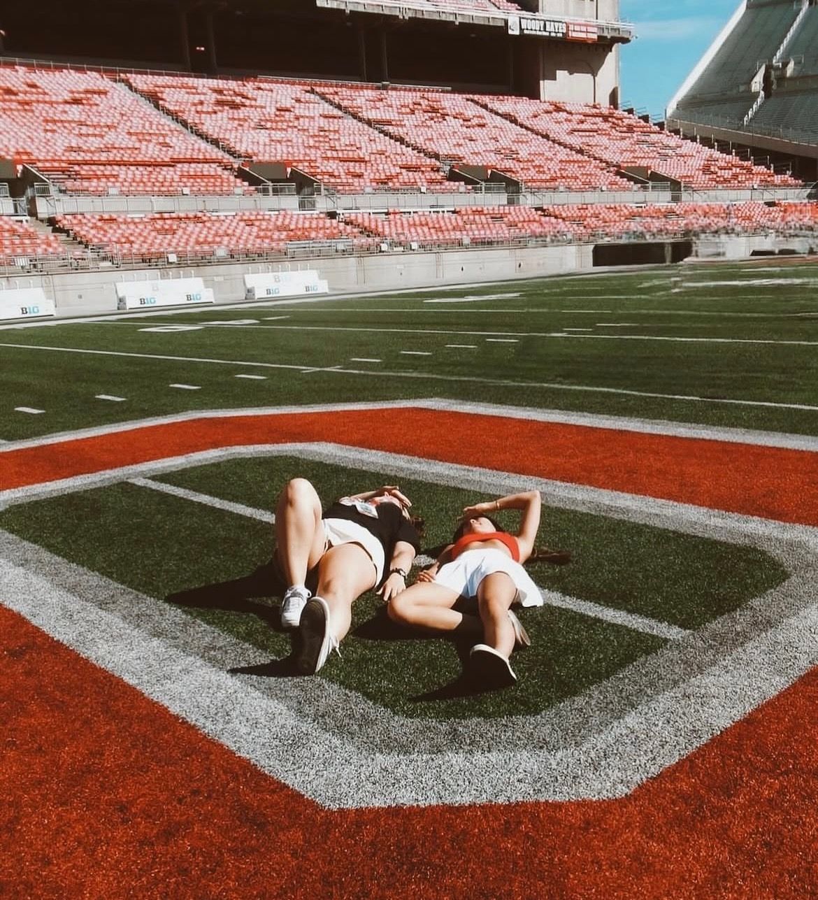 Two students lying on the Block “O” logo at Ohio Stadium, soaking up the sun on the field with empty red stadium seats in the background—just minutes from VERVE Columbus.