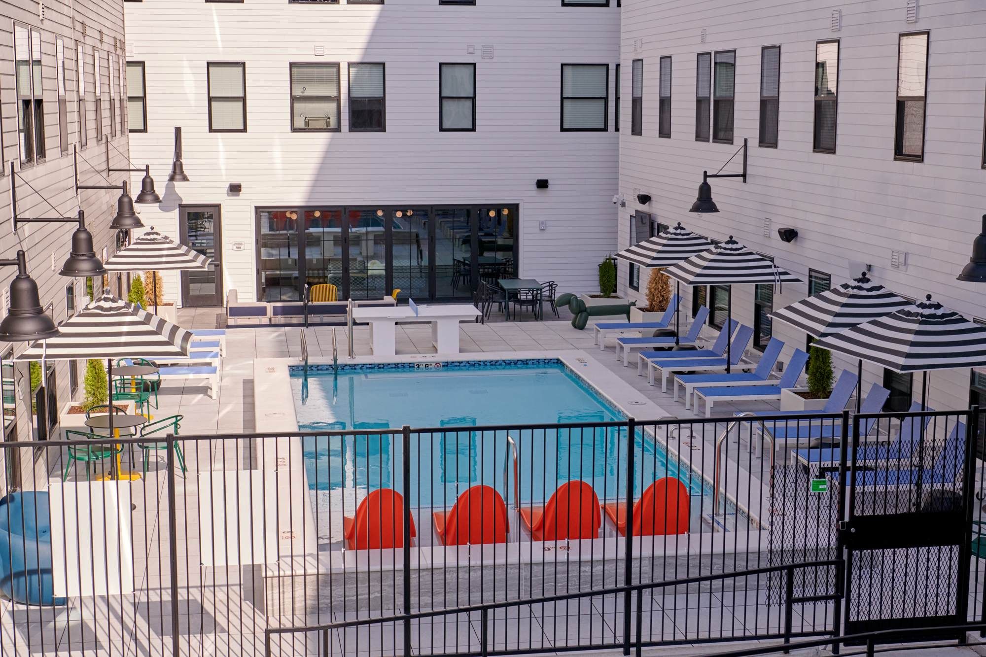 Evening view of the outdoor pool deck at VERVE Columbus, featuring modern lounge chairs, striped umbrellas, and a row of vibrant orange pool floats, creating a stylish and relaxing retreat.