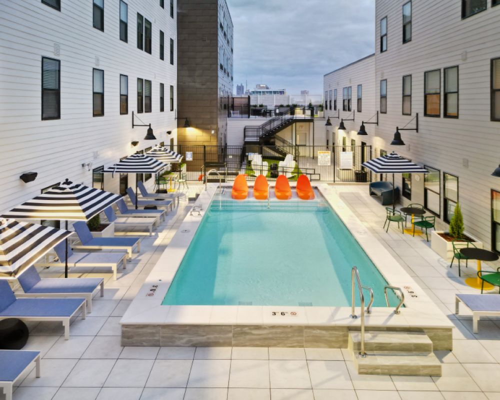 Evening view of the outdoor pool deck at VERVE Columbus, featuring modern lounge chairs, striped umbrellas, and a row of vibrant orange pool floats, creating a stylish and relaxing retreat.