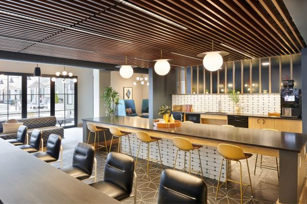 Chic co-working and lounge space at VERVE Columbus featuring a long communal table with modern yellow chairs, warm wood ceiling accents, and globe pendant lighting—perfect for studying or meeting with friends.
