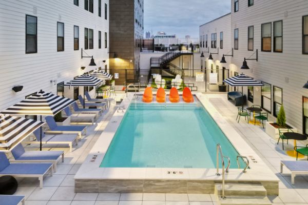 Evening view of the outdoor pool deck at VERVE Columbus, featuring modern lounge chairs, striped umbrellas, and a row of vibrant orange pool floats, creating a stylish and relaxing retreat.