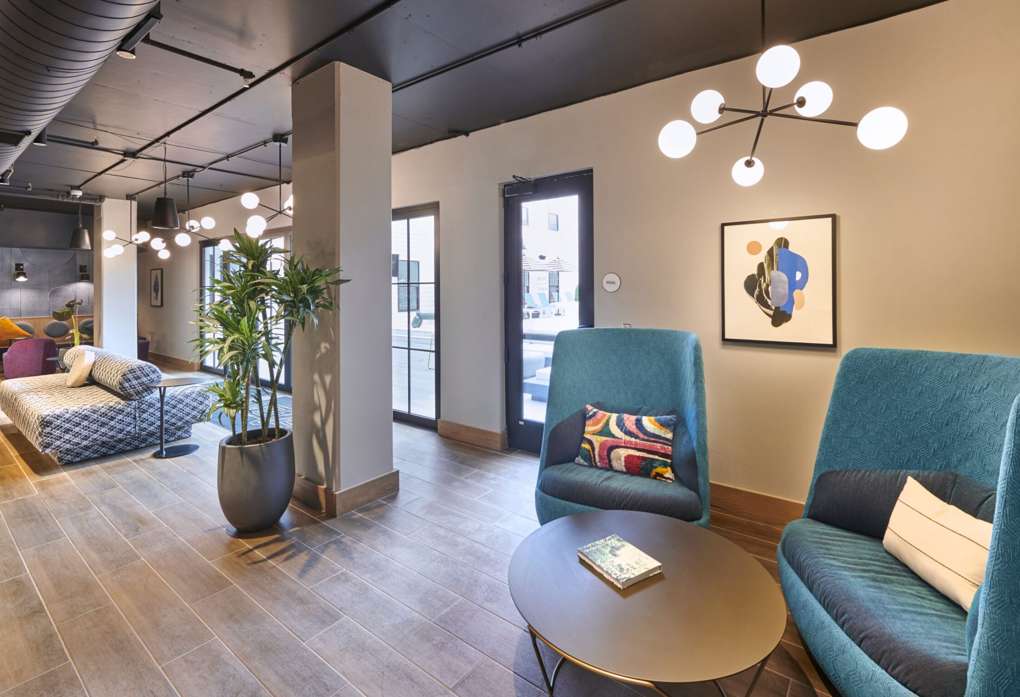 Stylish indoor lounge at VERVE Columbus featuring modern teal armchairs, a round coffee table, colorful accent pillows, and contemporary lighting—creating a cozy space for reading, relaxing, or casual conversation.