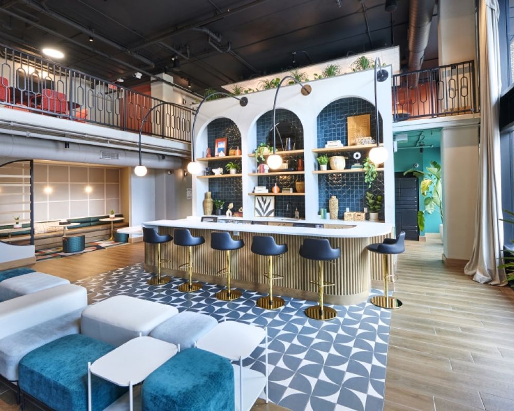 Stylish resident lounge at VERVE Columbus featuring a modern bar with blue arch shelving, gold accents, bold tile flooring, and plush seating designed for casual hangouts or study sessions.