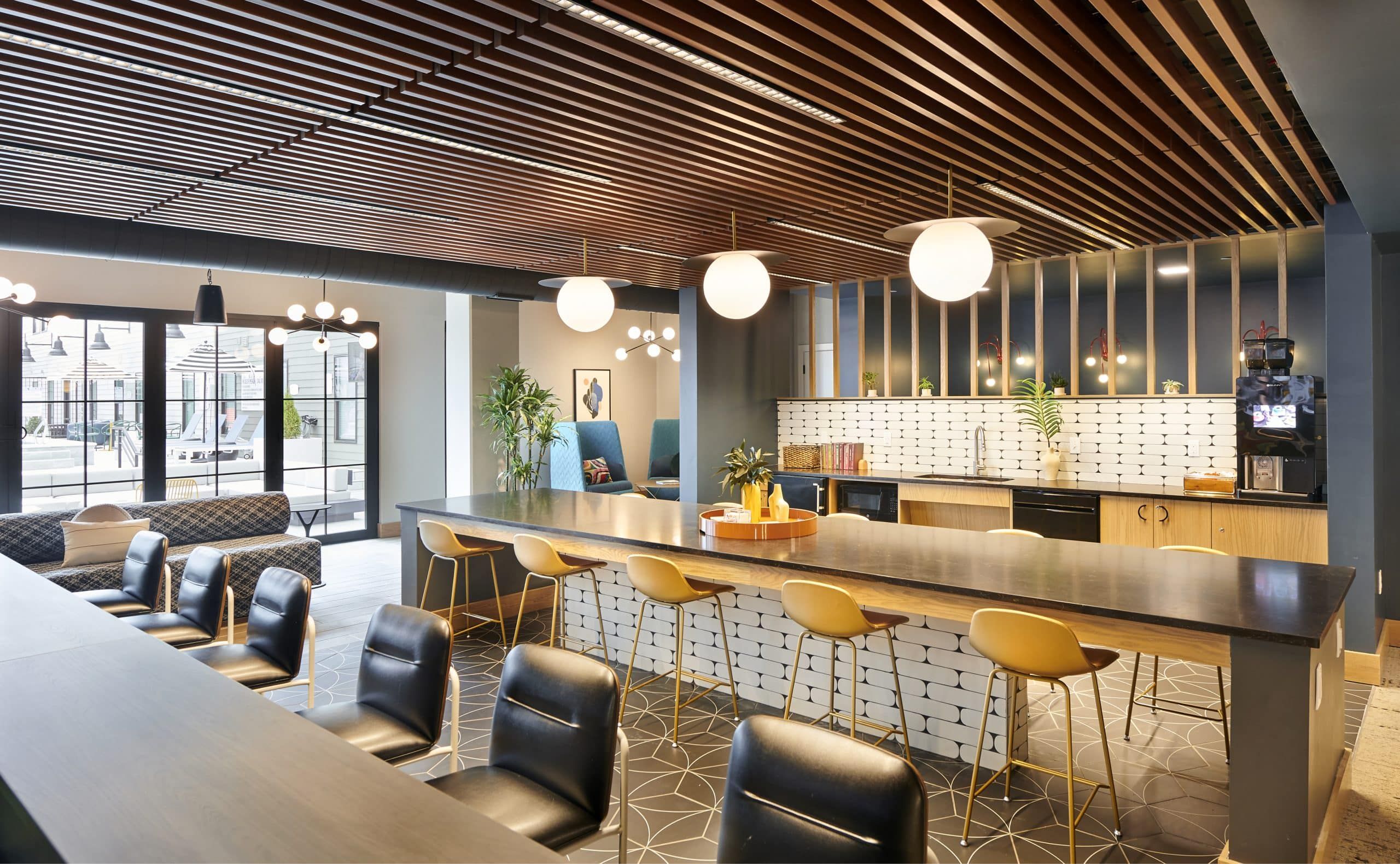 Chic co-working and lounge space at VERVE Columbus featuring a long communal table with modern yellow chairs, warm wood ceiling accents, and globe pendant lighting—perfect for studying or meeting with friends.